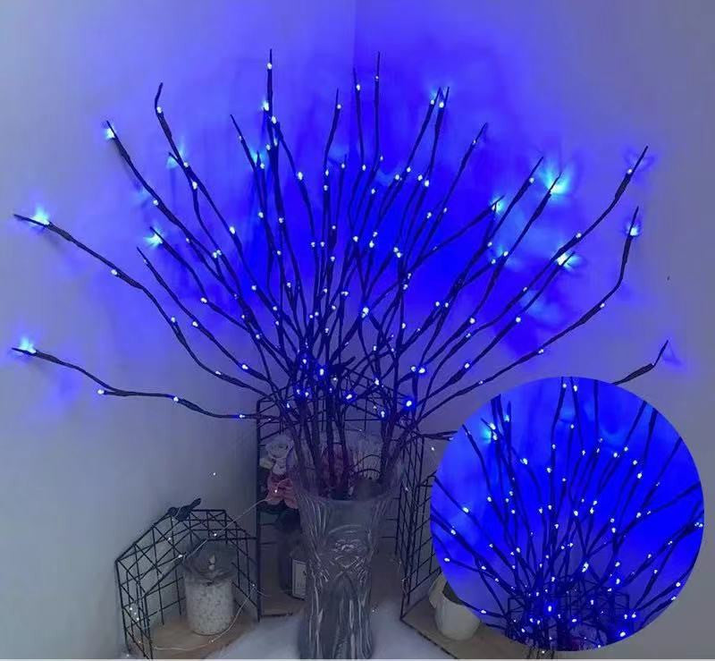 Decorative branch with blue LED lights in a clear vase against a white wall.
