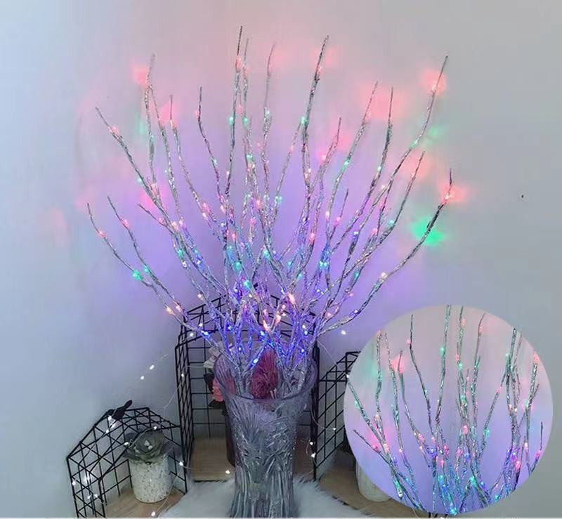 Decorative branch with colorful lights in a vase against a white wall.