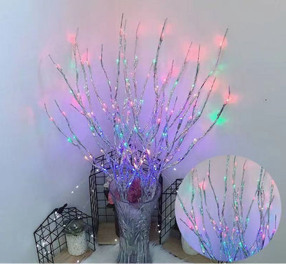 Decorative branch with colorful lights in a vase against a white wall.