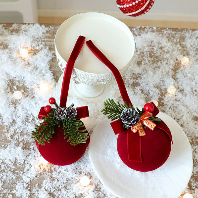 Two red Christmas ornaments with greenery and pinecones on a decorative surface.