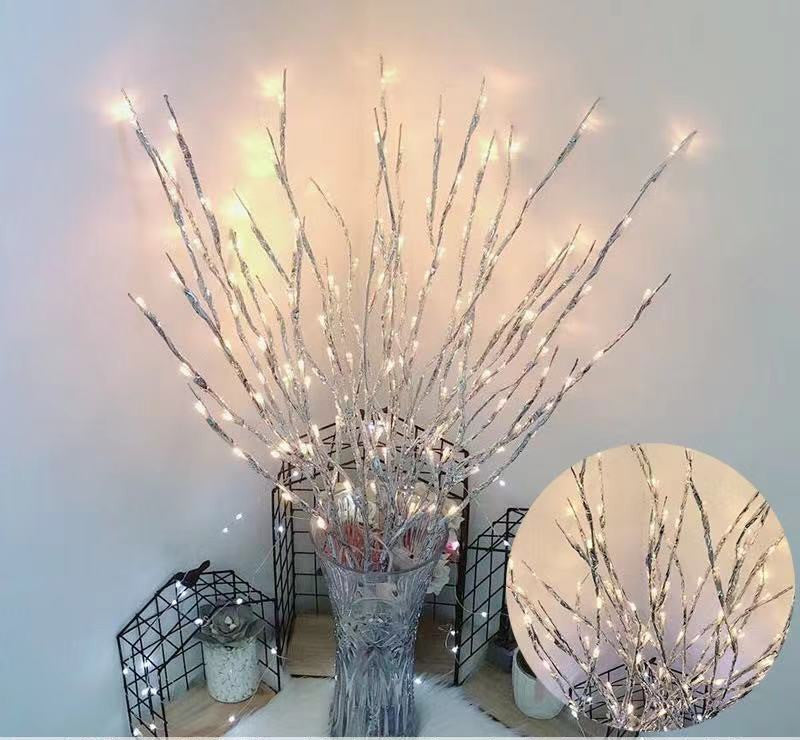 Decorative branches with LED lights in a vase against a white wall.