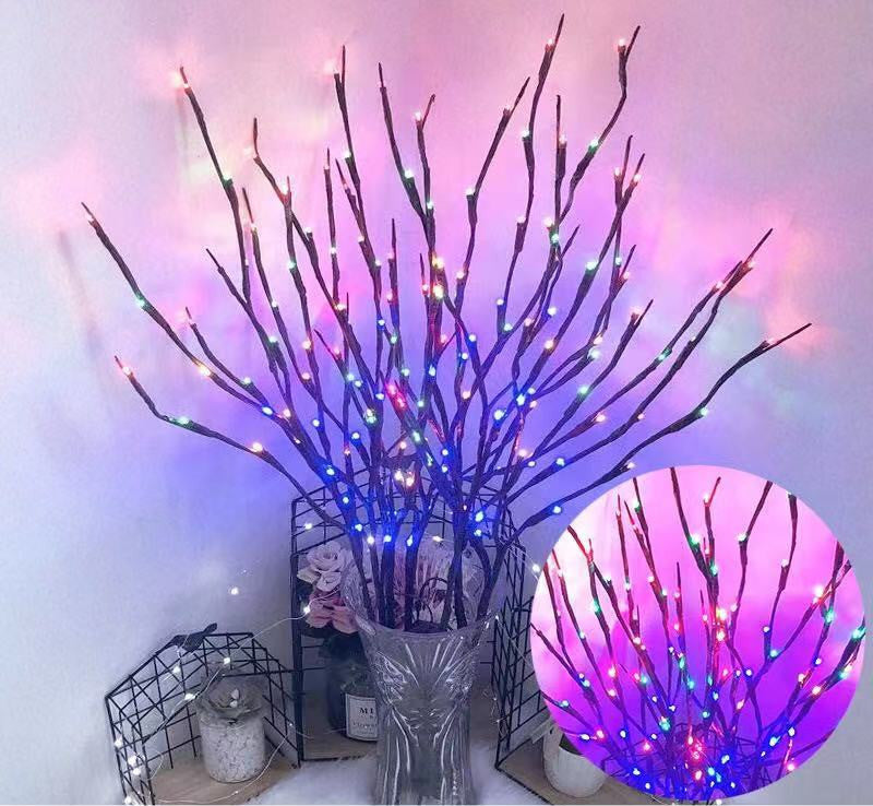 Decorative branches with colorful LED lights in a clear vase against a white wall.