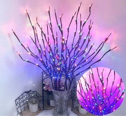 Decorative branches with colorful LED lights in a clear vase against a white wall.
